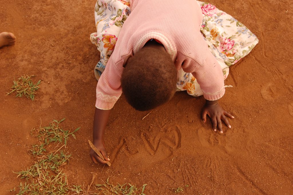 Flicka skriver i sanden.